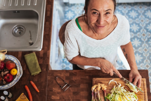 A woman is efficiently chopping vegetables in a compact kitchen.